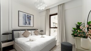 Een moderne slaapkamer met een groot bed, nachtkastjes, een lijstwerk, een raam met gordijnen en een potplant.