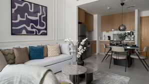 Een moderne woonkamer met een bank, salontafel en abstracte kunst. Deze leidt naar een keuken met houten kasten en apparatuur.
