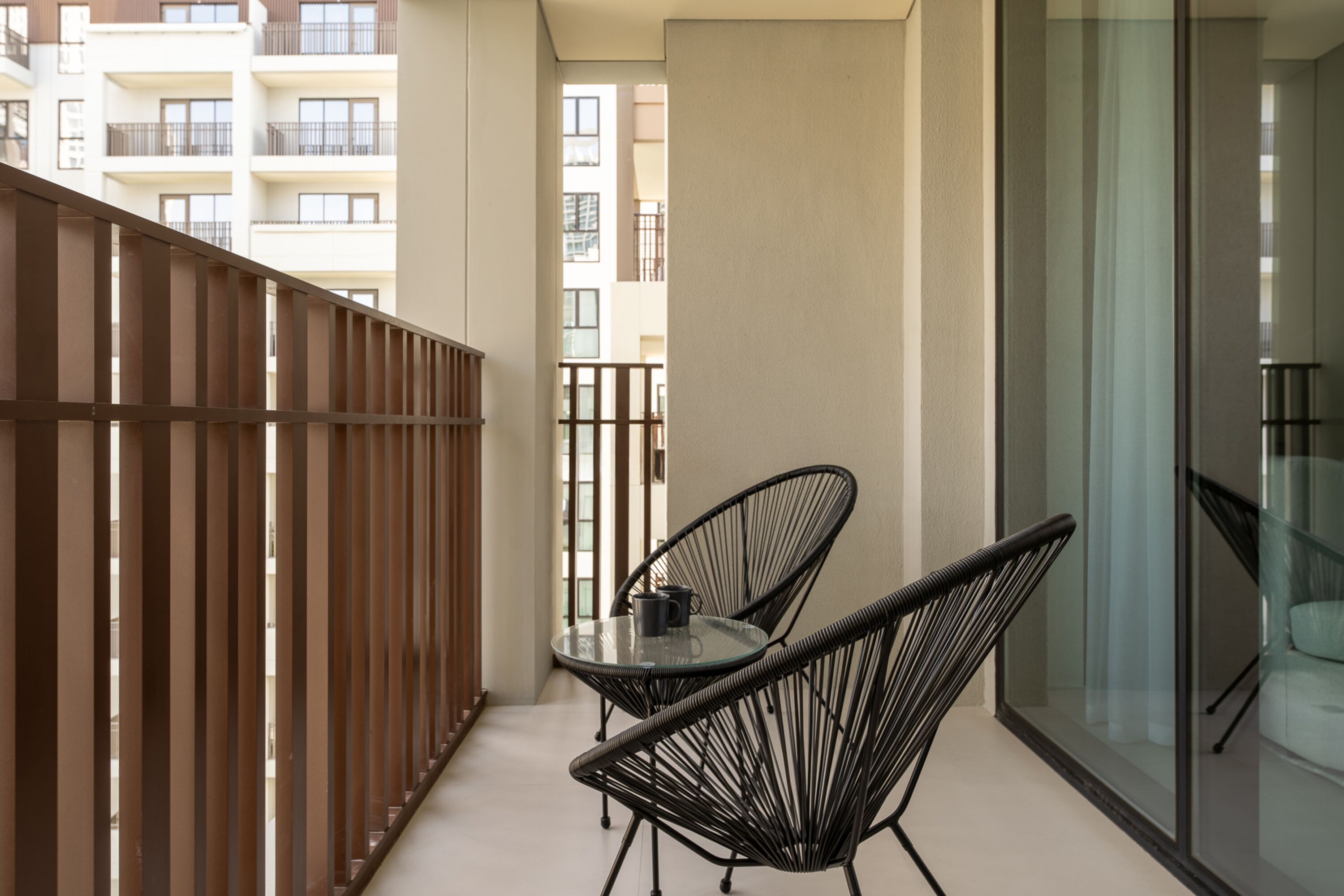 A balcony with two black chairs, a glass table, and a view of a building in the background.