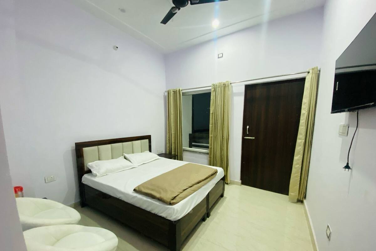 A bedroom with a bed, a ceiling fan, a window with curtains, and a TV mounted on the wall.