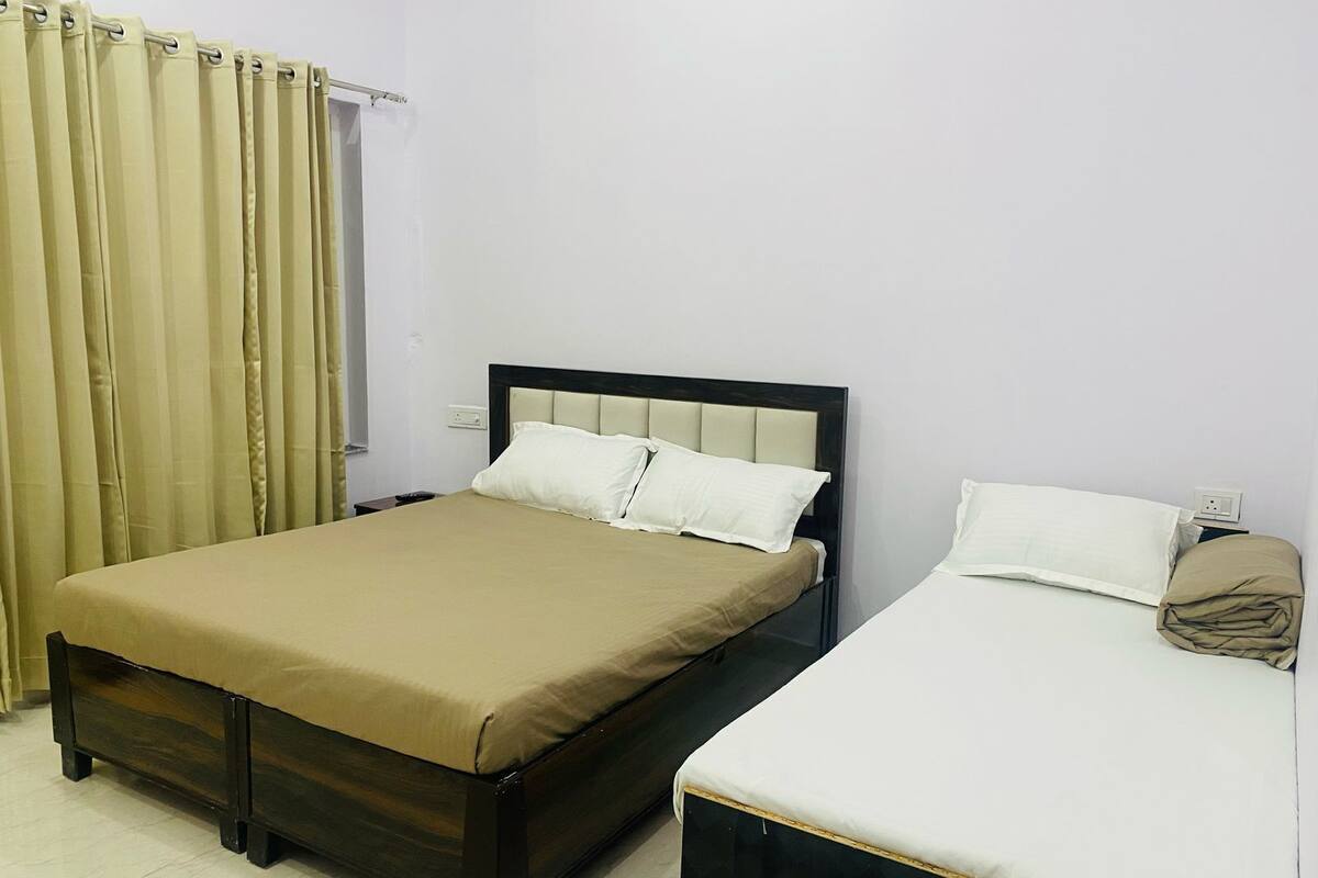 A room with two beds, one with a dark frame and beige bedding, and the other with a white frame and white bedding.