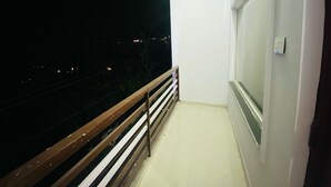 Een balkon met een metalen hekwerk, een raam en uitzicht op het verlichte stadsbeeld 's nachts.