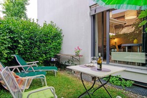 Une terrasse avec deux fauteuils de jardin verts, une petite table sur laquelle se trouve une bouteille de vin et une plante en pot.