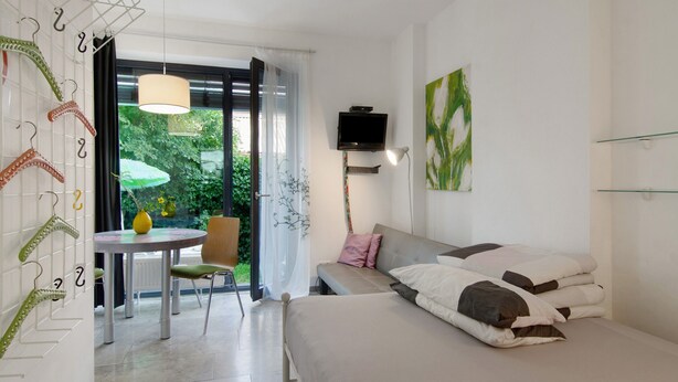 Een slaapkamer met een bed, een televisie, een tafel met stoelen en uitzicht op groen.