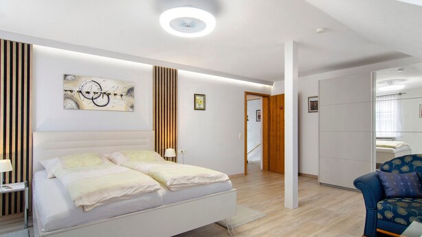 A modern bedroom with a bed, a chair, and a painting on the wall.