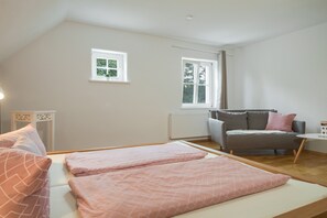 A bedroom with two beds, a grey sofa, and two windows. - Apartment 'Mit Giebelzimmer' with Shared Garden and Wi-Fi (Ravensburg)