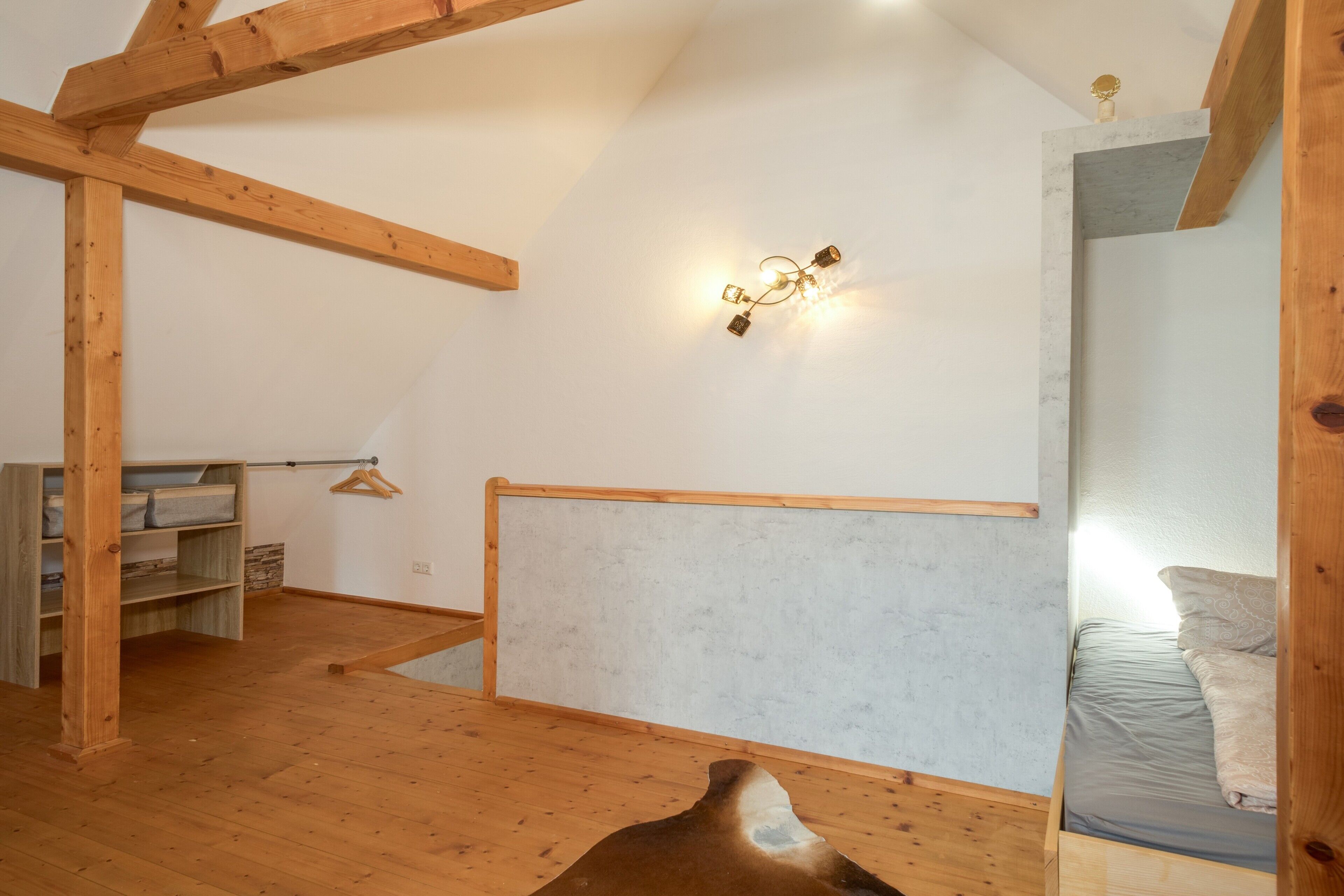 Et værelse med træbjælker, en seng, en hængende lampe og et garderobeskab.