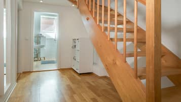 Eine Holztreppe führt zu einer oberen Etage, ein Badezimmer mit Dusche und ein Flur mit einer Tür zu einem weiteren Raum.