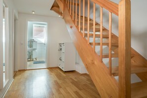 A wooden staircase leading to an upper floor, a bathroom with a shower, and a hallway with a door leading to another room. - Apartment 'Mit Giebelzimmer' with Shared Garden and Wi-Fi (Ravensburg)