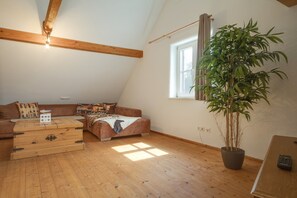 Une pièce de style « loft », avec un plafond en pente, des poutres en bois, une grande fenêtre, un canapé, une commode et une plante en pot.