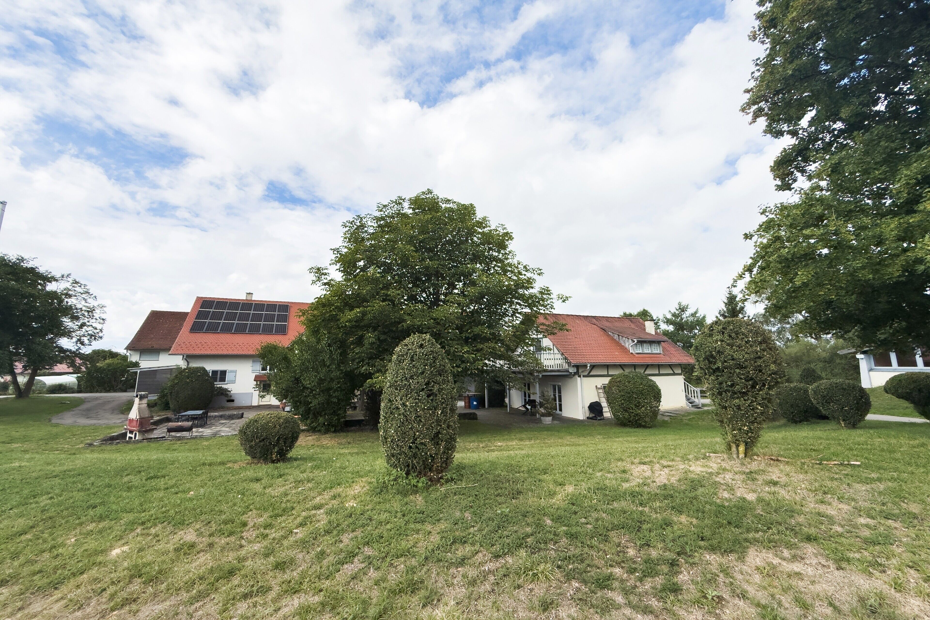 A house with a red roof, surrounded by well-maintained lawns and trees.