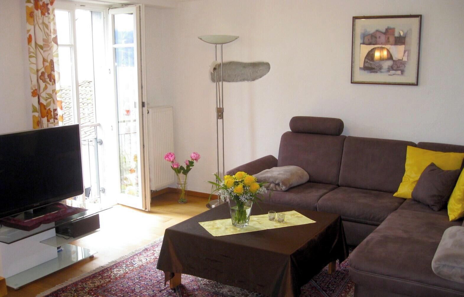 Una sala de estar con un sofá, una mesa de centro con flores, un televisor y un cuadro en la pared.