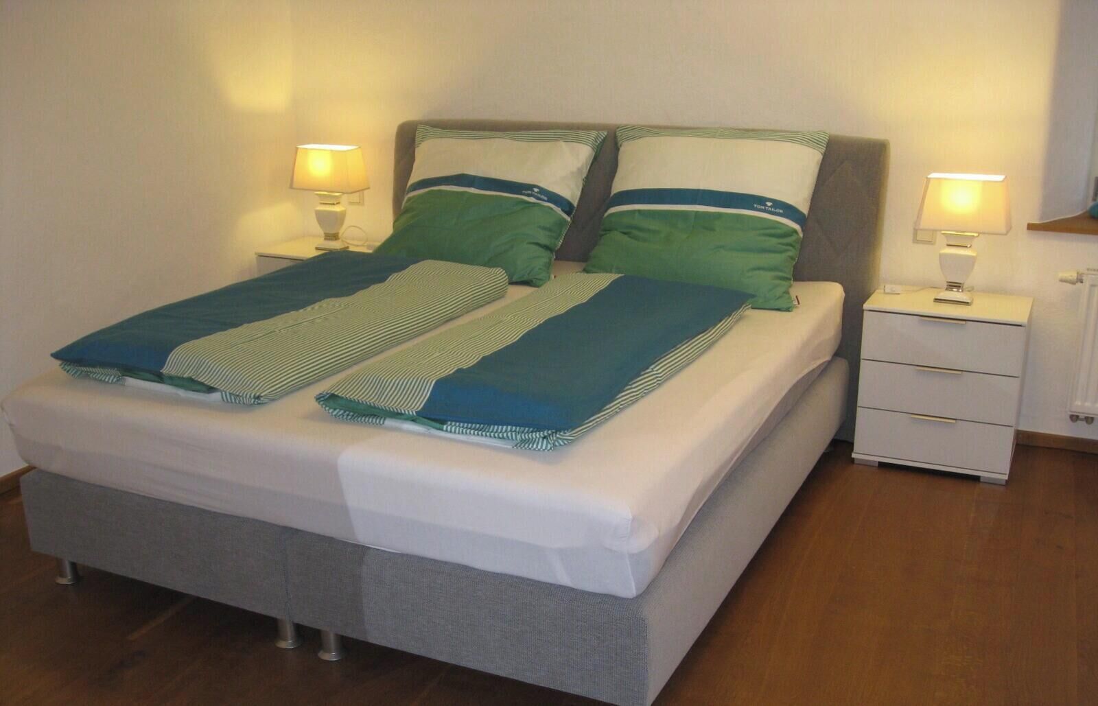 Een bed met een grijs frame, twee nachtkastjes en een nachtkastje met een lamp.