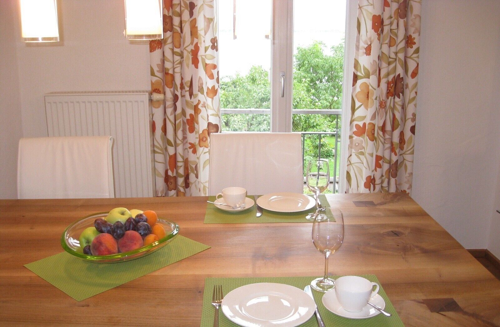 Een eettafel gedekt met borden, bestek, een schaal fruit en een wijnglas.