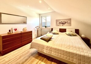 Quarto com uma cama grande, cômoda, espelho e janela.