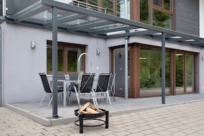 Un patio moderno al aire libre con cerramiento de vidrio, una mesa con sillas y un brasero.