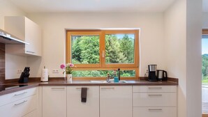A modern kitchen with white cabinets, a wooden countertop, a window with a view of trees, and a coffee maker.