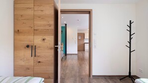 A bedroom with a wooden wardrobe, a coat rack, and a bed with striped bedding.