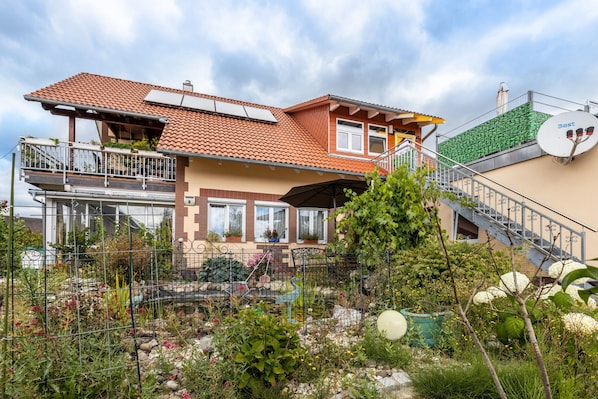 A two-story house with a balcony, a satellite dish, and a garden in front.