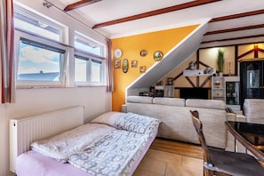 A bedroom with a bed, a sofa, a dining table, and a staircase leading to an upper level.