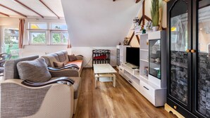 Een woonkamer met een bank, televisie, wit kastje en houten vloer.