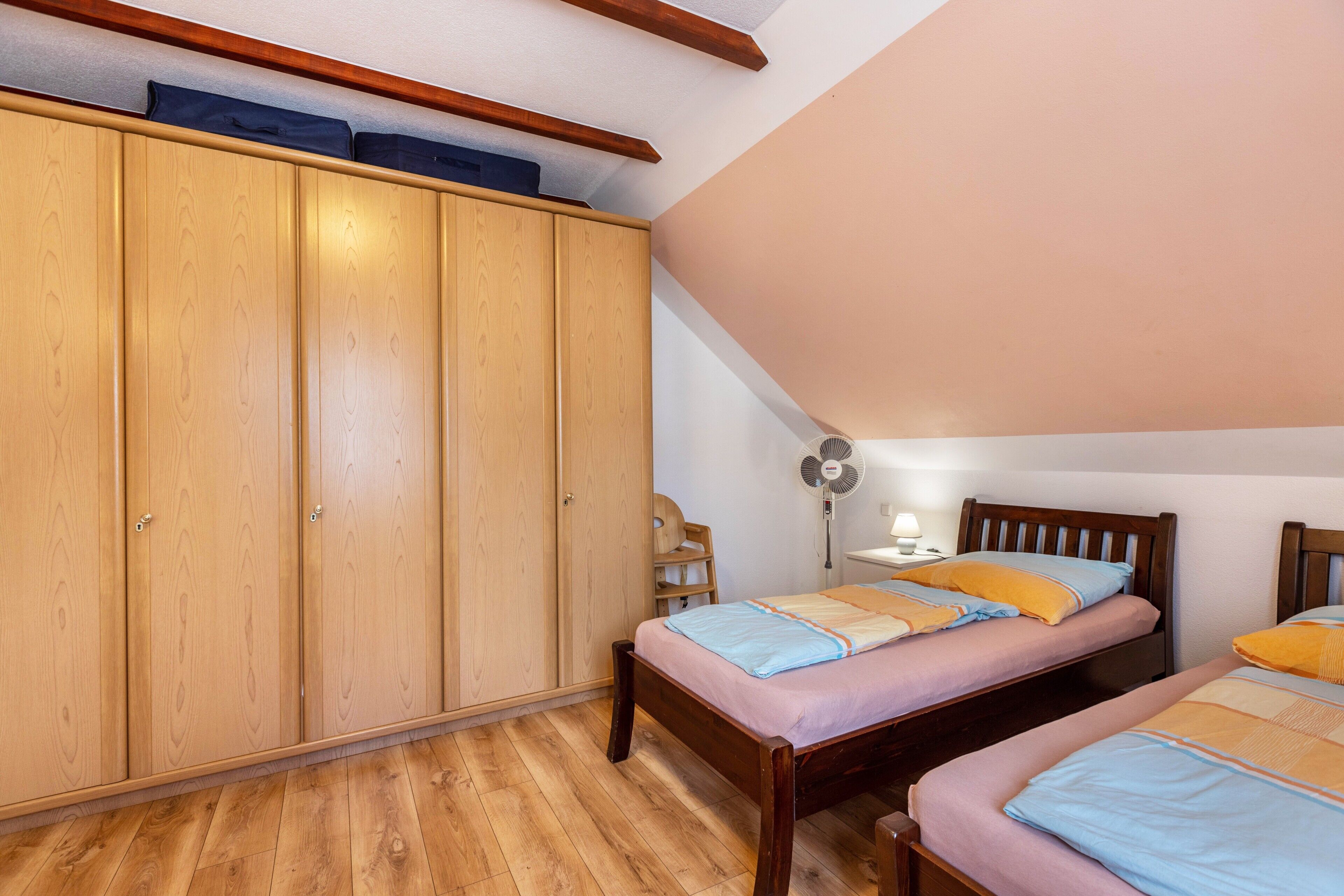A bedroom with two single beds, wooden wardrobe, and a ceiling fan.