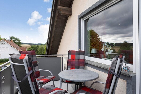 Un balcon avec deux chaises et une table, une fenêtre donnant sur la campagne et une maison en arrière-plan.