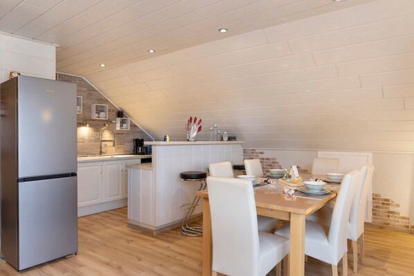 A modern kitchen with a built-in island, white cabinetry, and a dining area with a wooden table and white chairs.