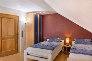 Une chambre avec un plafond en pente, une armoire, deux lits, des tables de chevet et une lampe.