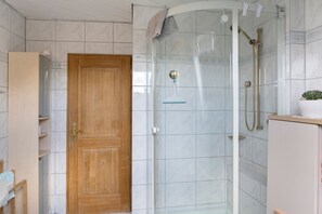 Une salle de bain avec une douche, une porte en bois et un mur recouvert de carreaux blancs.