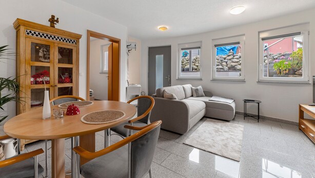 A modern living room with a sofa, a dining table with chairs, a cabinet with glass doors, and a view of the outside through windows. - Apartment 'In Der Vulkan-Eifel' with Wi-Fi (Mendig)