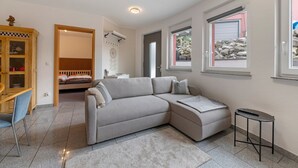 A modern living room with a sofa, a small table, a chair, a wooden cabinet, and a bed in the background. - Apartment 'In Der Vulkan-Eifel' with Wi-Fi (Mendig)