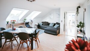 A modern living room with a dark grey sofa, a glass dining table with chairs, and a skylight above. - Apartment 'Wadee' with Lake View, Balcony and Wi-Fi (Radolfzell am Bodensee)