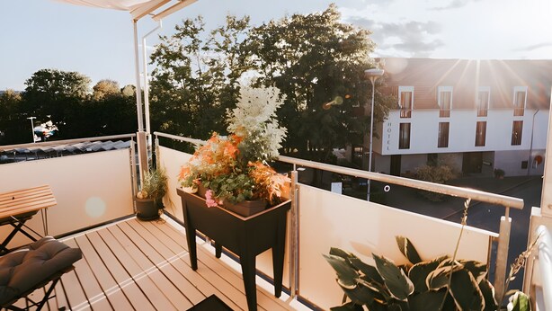 A balcony with a wooden table and chairs, a potted plant, and a view of a building with a sign that reads 'HOTEL.' - Apartment 'Wadee' with Lake View, Balcony and Wi-Fi (Radolfzell am Bodensee)