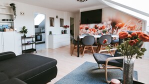 A modern living room with a sofa, chairs, a dining table, and a kitchen in the background. - Apartment 'Wadee' with Lake View, Balcony and Wi-Fi (Radolfzell am Bodensee)