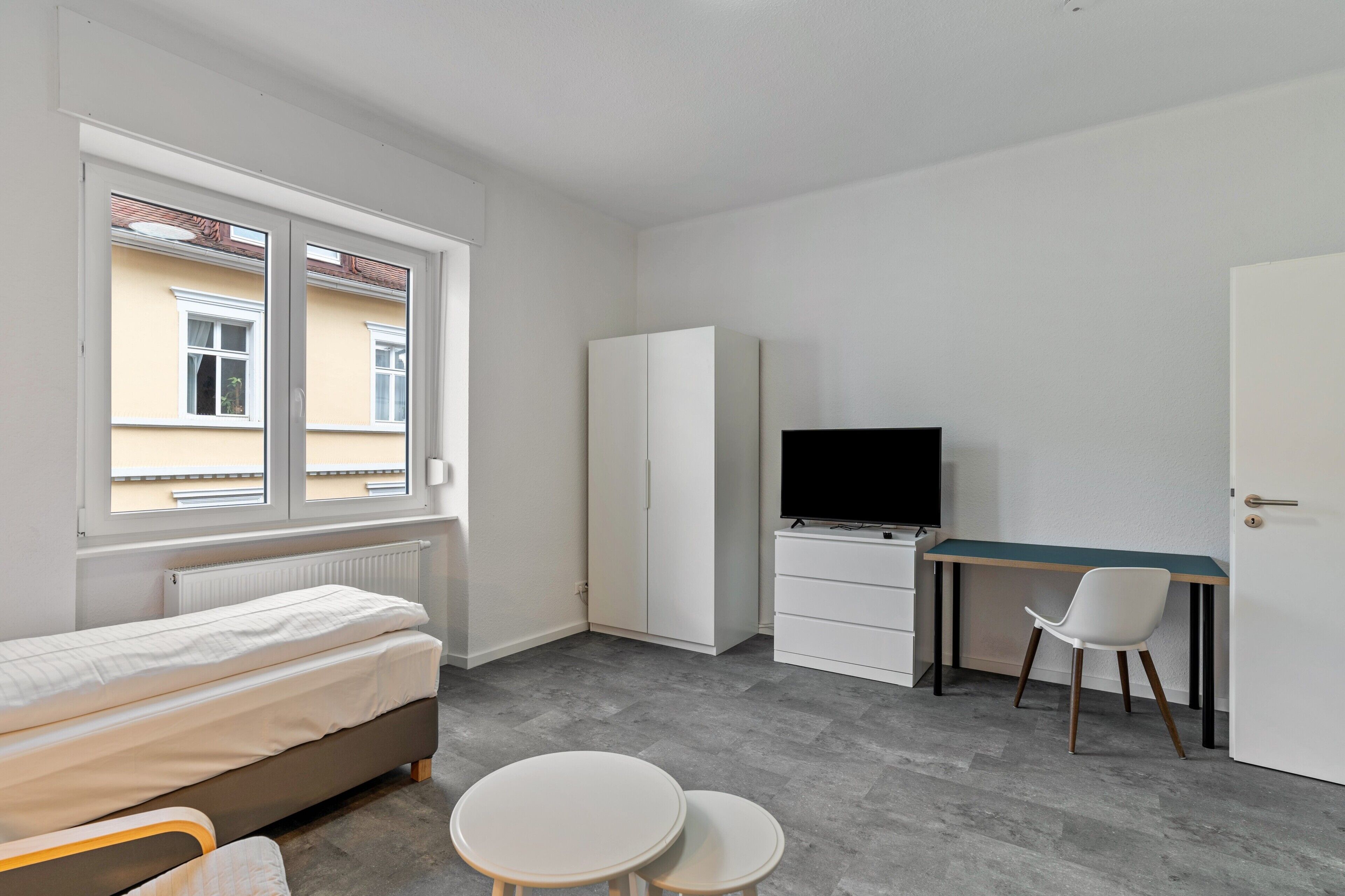 A bedroom with a bed, a desk, a chair, and a TV.