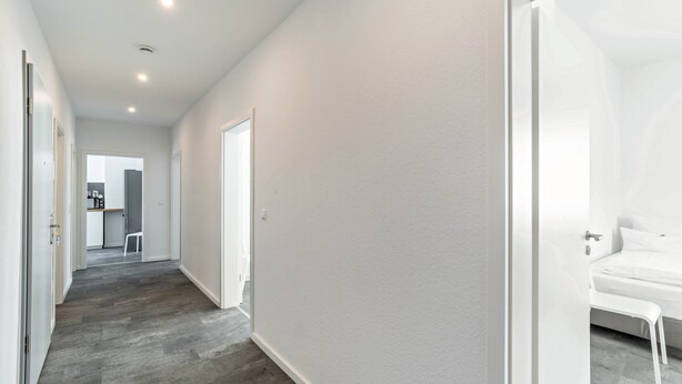 A hallway with a bed, a chair, and a desk in the background. - Holiday Apartment '1st Floor Left' with Balcony and Wi-Fi (Pforzheim)