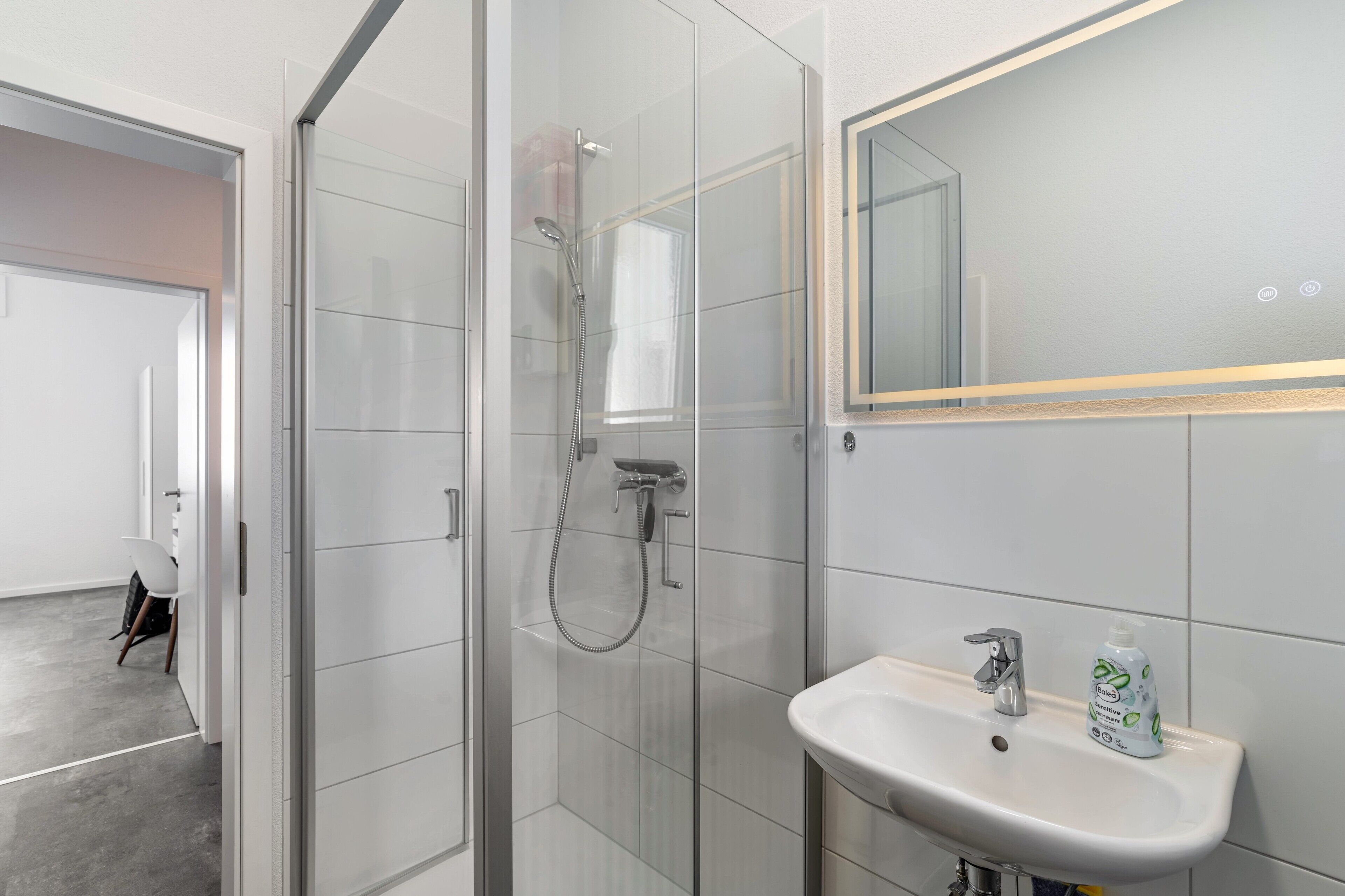 A modern bathroom with a glass-enclosed shower, a white sink, and a mirror with a gold frame.