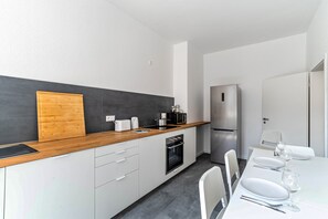 A modern kitchen with white cabinets, a wooden countertop, a built-in oven, a refrigerator, and a dining area with a table set for two.