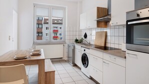A modern kitchen with a built-in washing machine, a dining area with a table set for four, and a view of the outside balcony. - Apartment '2nd Floor Left' with Wi-Fi (Pforzheim)