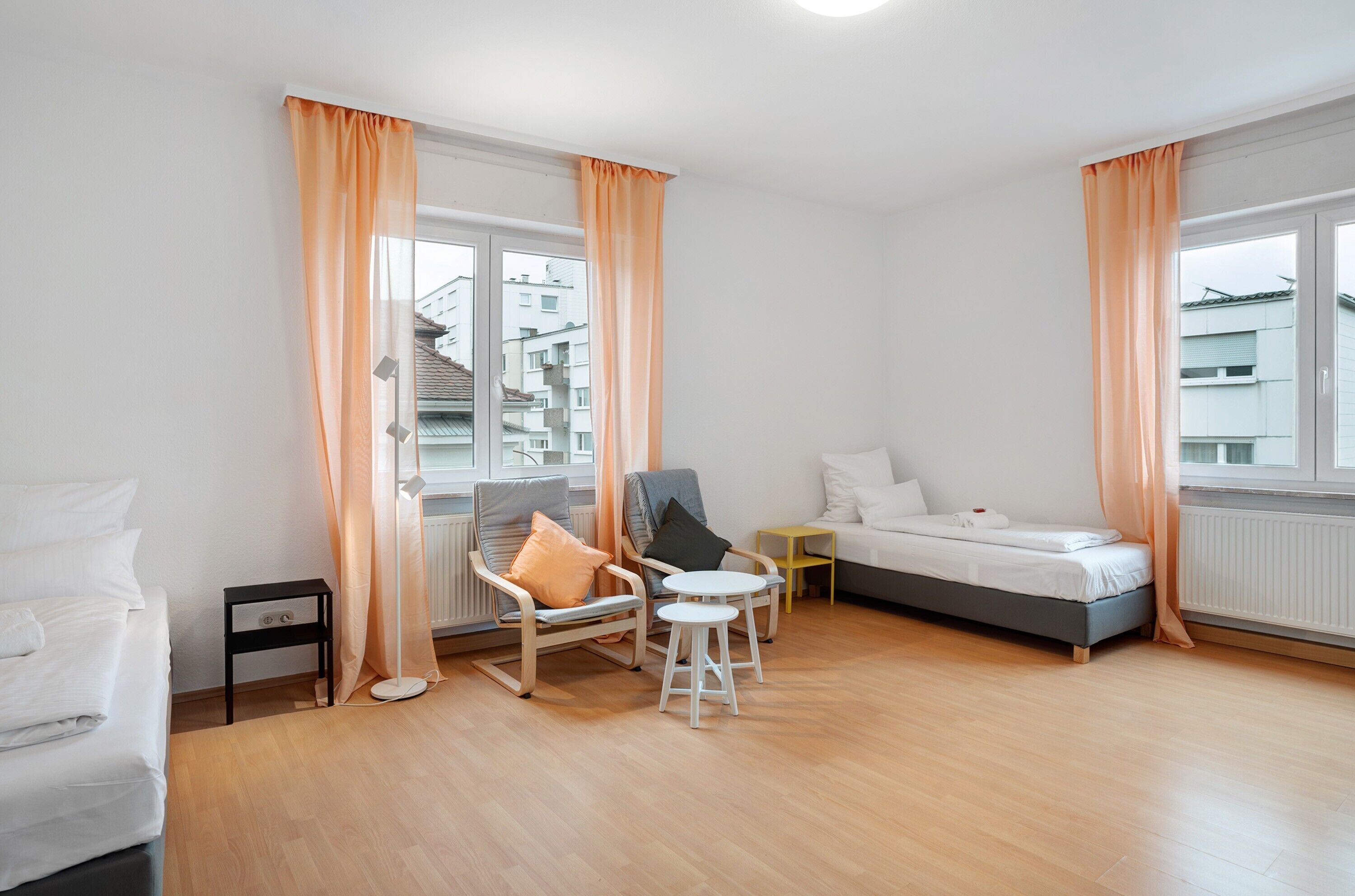 Ein Zimmer mit einem Bett, zwei Stühlen, einem kleinen Tisch und einem Fenster mit Vorhängen.