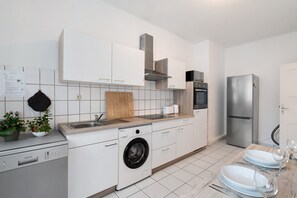 Eine moderne Küche mit weißen Schränken, einer integrierten Waschmaschine, einem Edelstahlkühlschrank und einer Holz Arbeitsplatte.