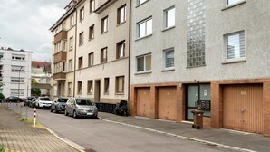 A street with parked cars, a trash bin, and a building with a garage door. - Apartment '2nd Floor Left' with Wi-Fi (Pforzheim)