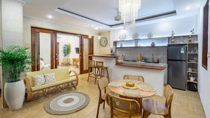 A modern kitchen with a built-in island, a dining area with a round table and chairs, and a living area with a sofa and a large potted plant. -  Umber Rise Villa (Bali)