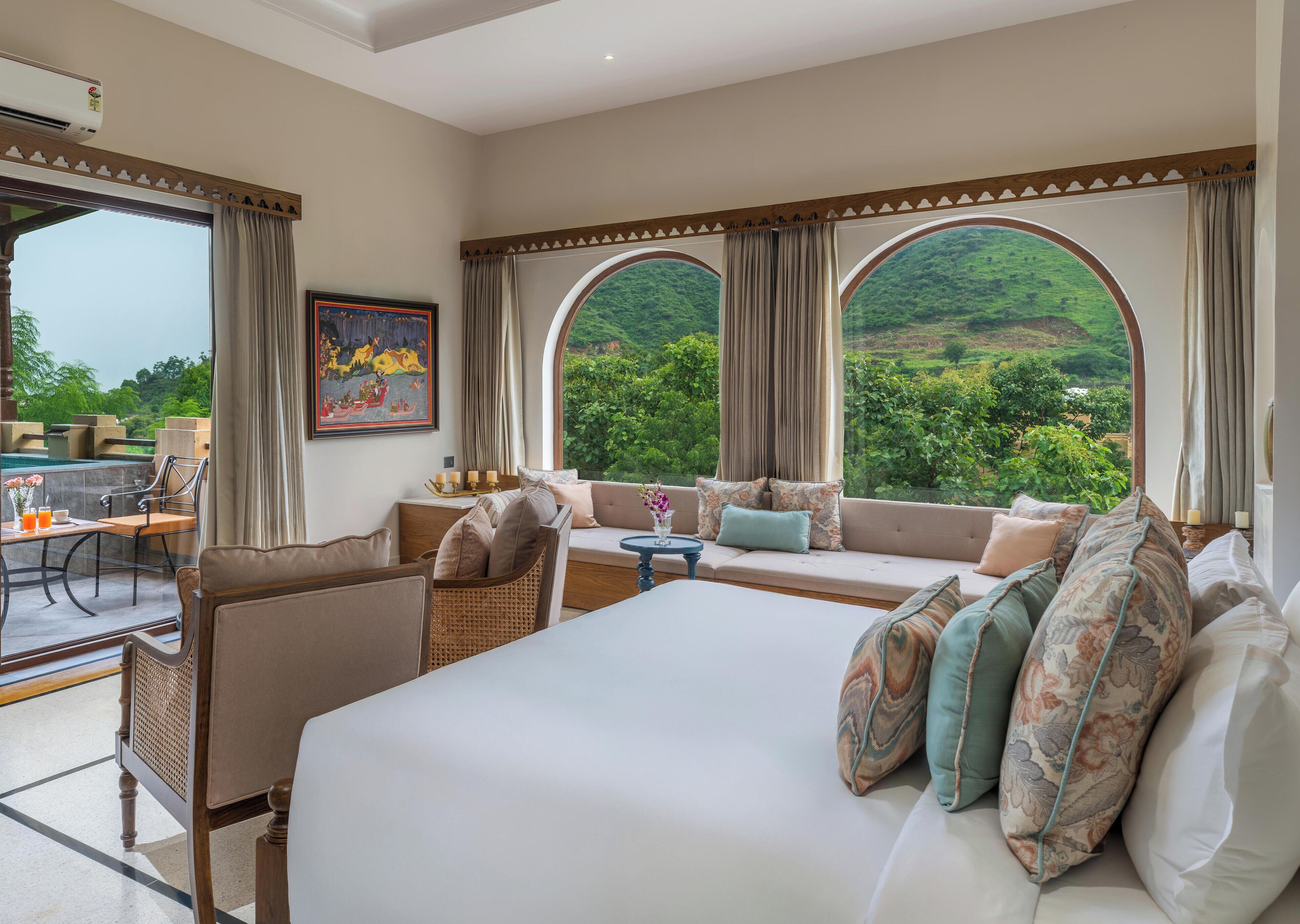 Ein Hotelzimmer mit einem großen Bett, einer Couch, einem Essbereich und Blick auf eine üppige grüne Landschaft.