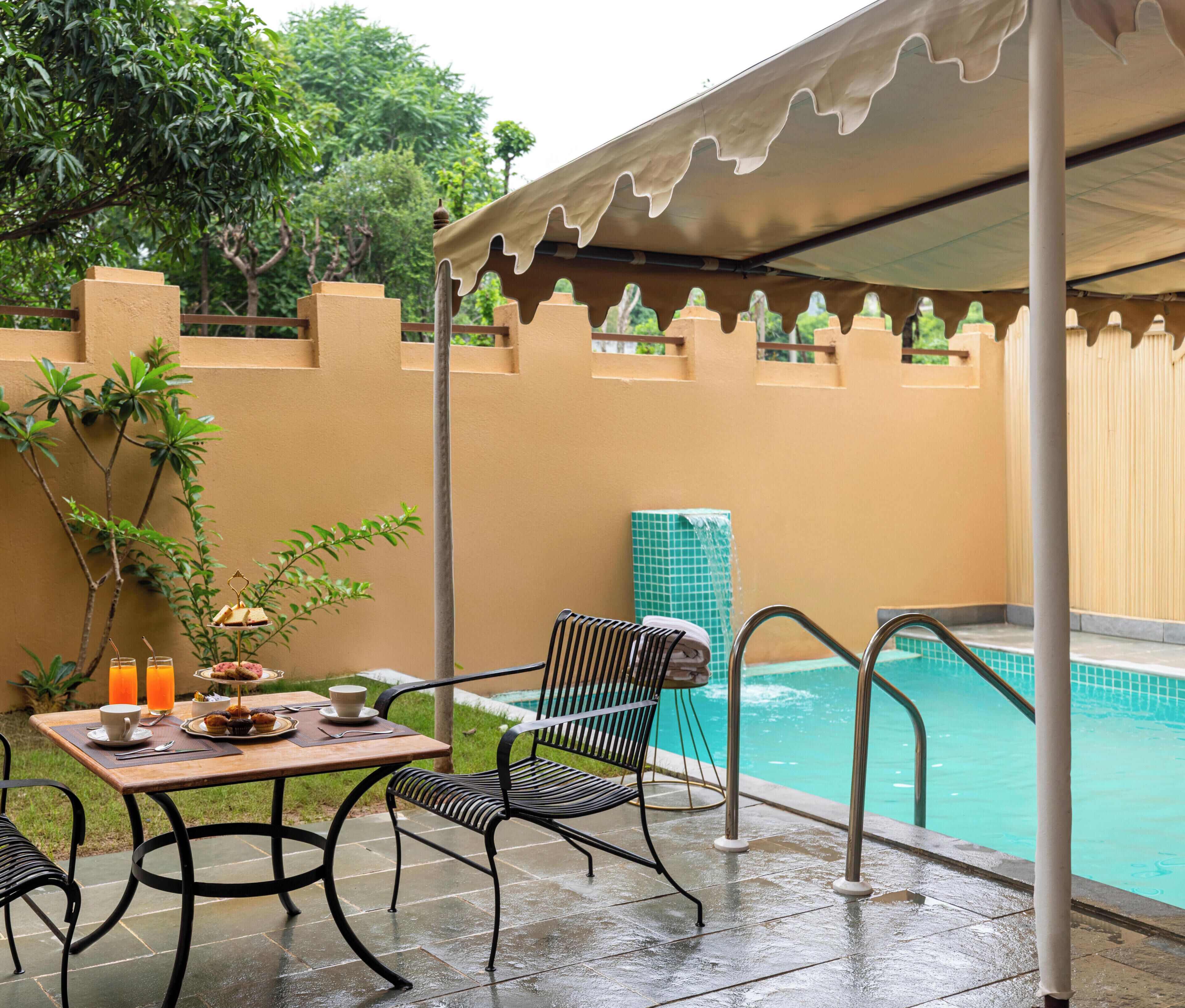 Un patio techado con piscina, una mesa con alimentos para el desayuno y una silla.
