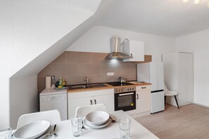 Cocina compacta con lavavajillas, estufa, horno y una pequeña zona de comedor con mesa y sillas.