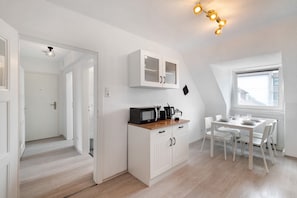 Cocina compacta con armarios blancos, una mesa de comedor con sillas y una ventana que proporciona luz natural.