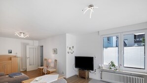 A modern living room with a sofa, a television, a radiator, and a window with blinds.