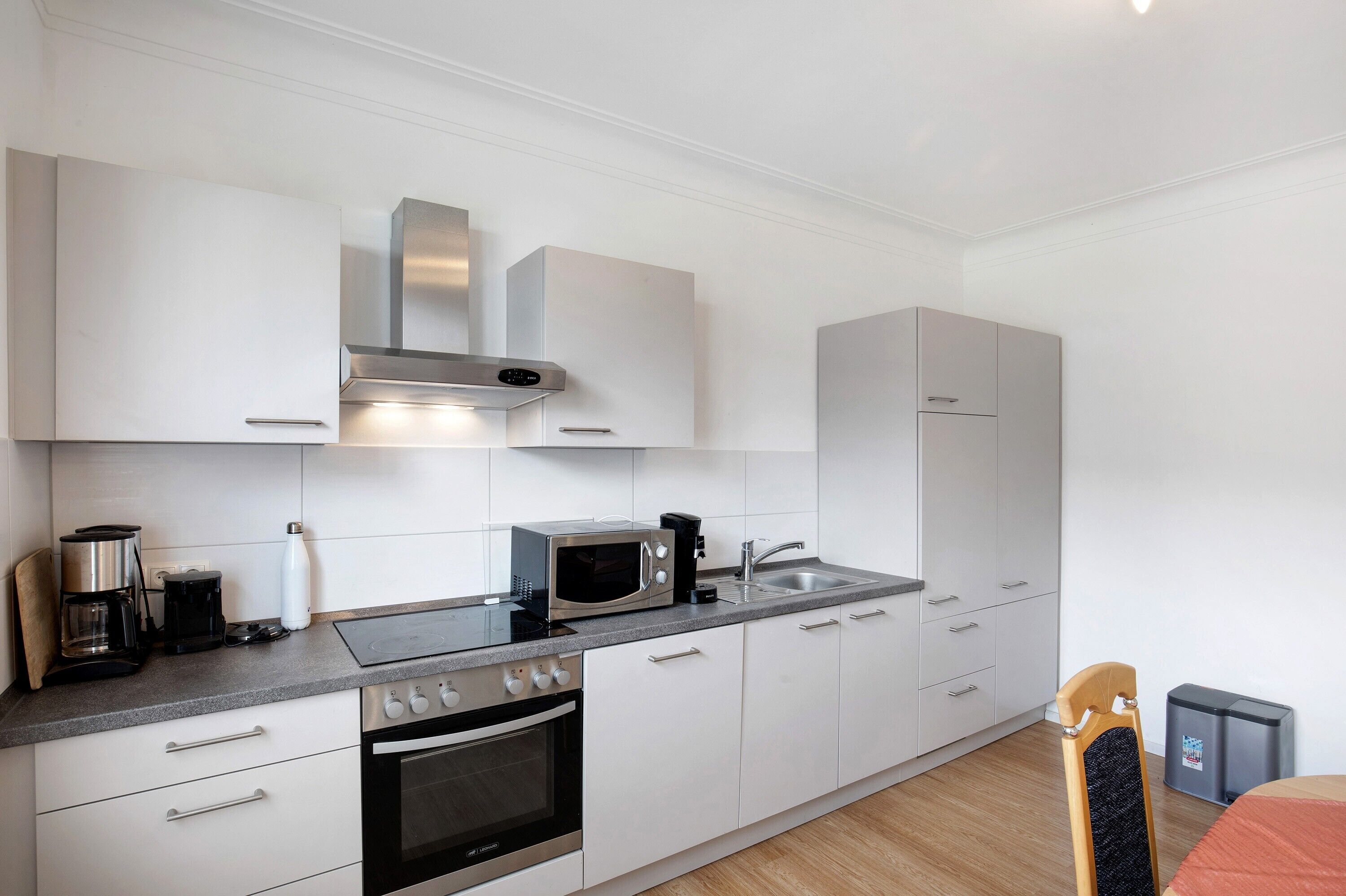 Una cocina moderna con armarios blancos, electrodomésticos de acero inoxidable y una silla de madera.